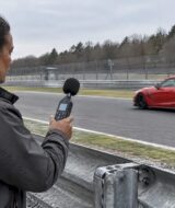 Red sports car passes a trackside sound marshal