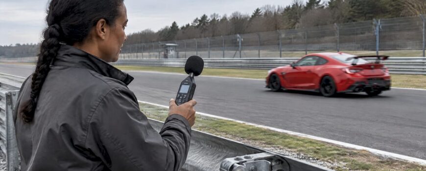 Red sports car passes a trackside sound marshal